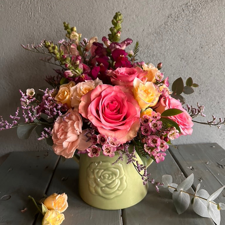 Bouquet of pink and yellow flowers in a green vase on a wooden surface.