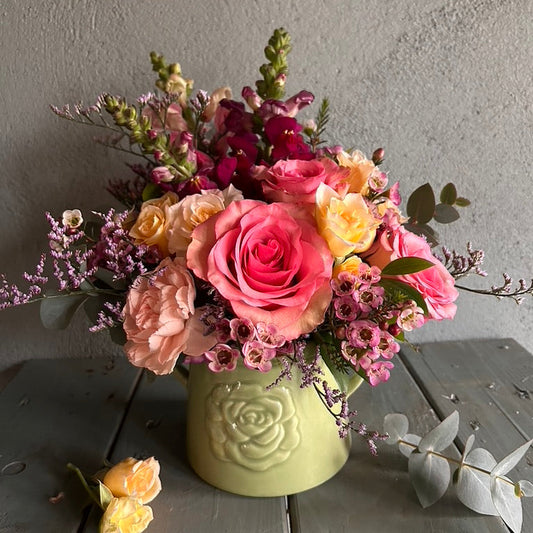 Bouquet of pink and yellow flowers in a green vase on a wooden surface.