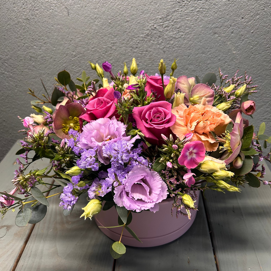 Colorful flower arrangement in a purple container on a wooden surface with a gray background