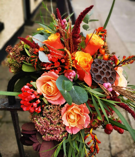 A vibrant Autumn-themed bouquet featuring a variety of flowers including oranges, reds, yellows, and greens, arranged to evoke the warm hues of a golden sunset.