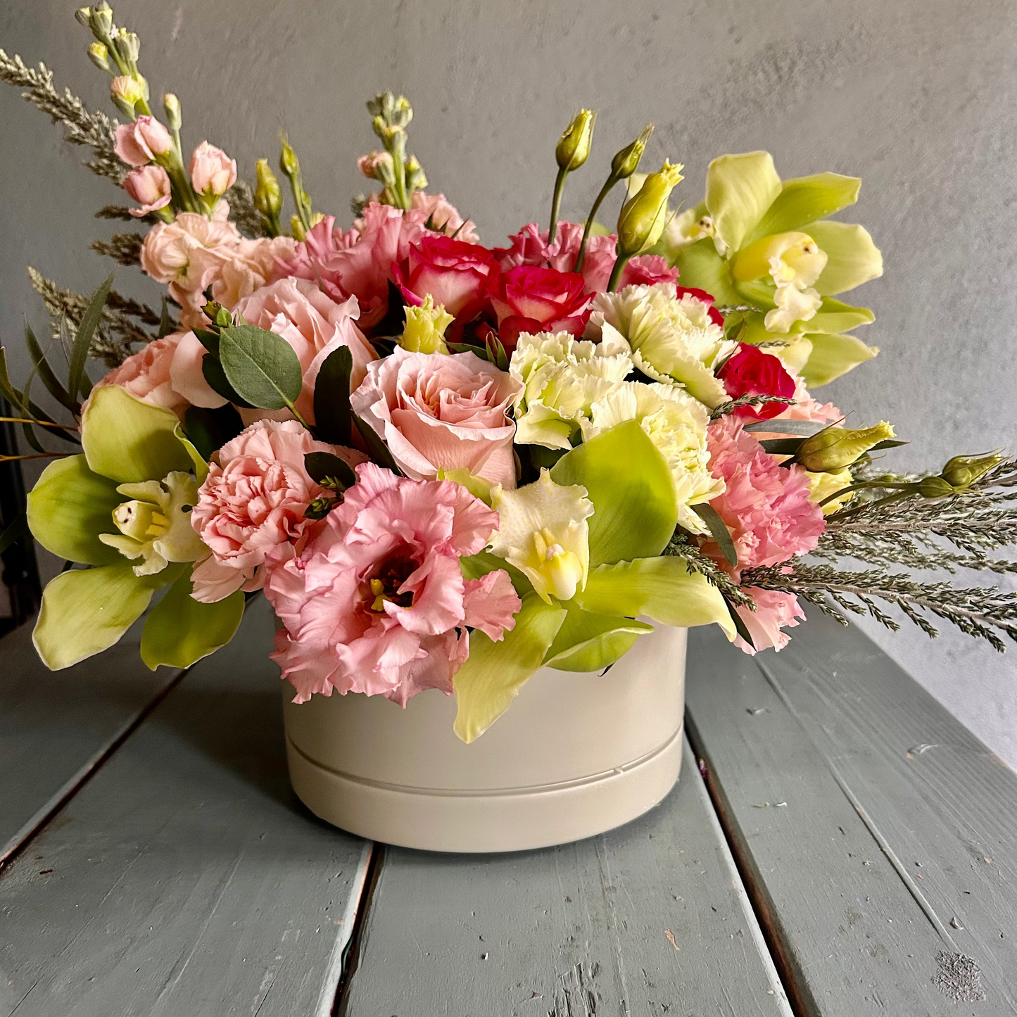 Floral arrangement in a white container on a wooden surface with a gray background