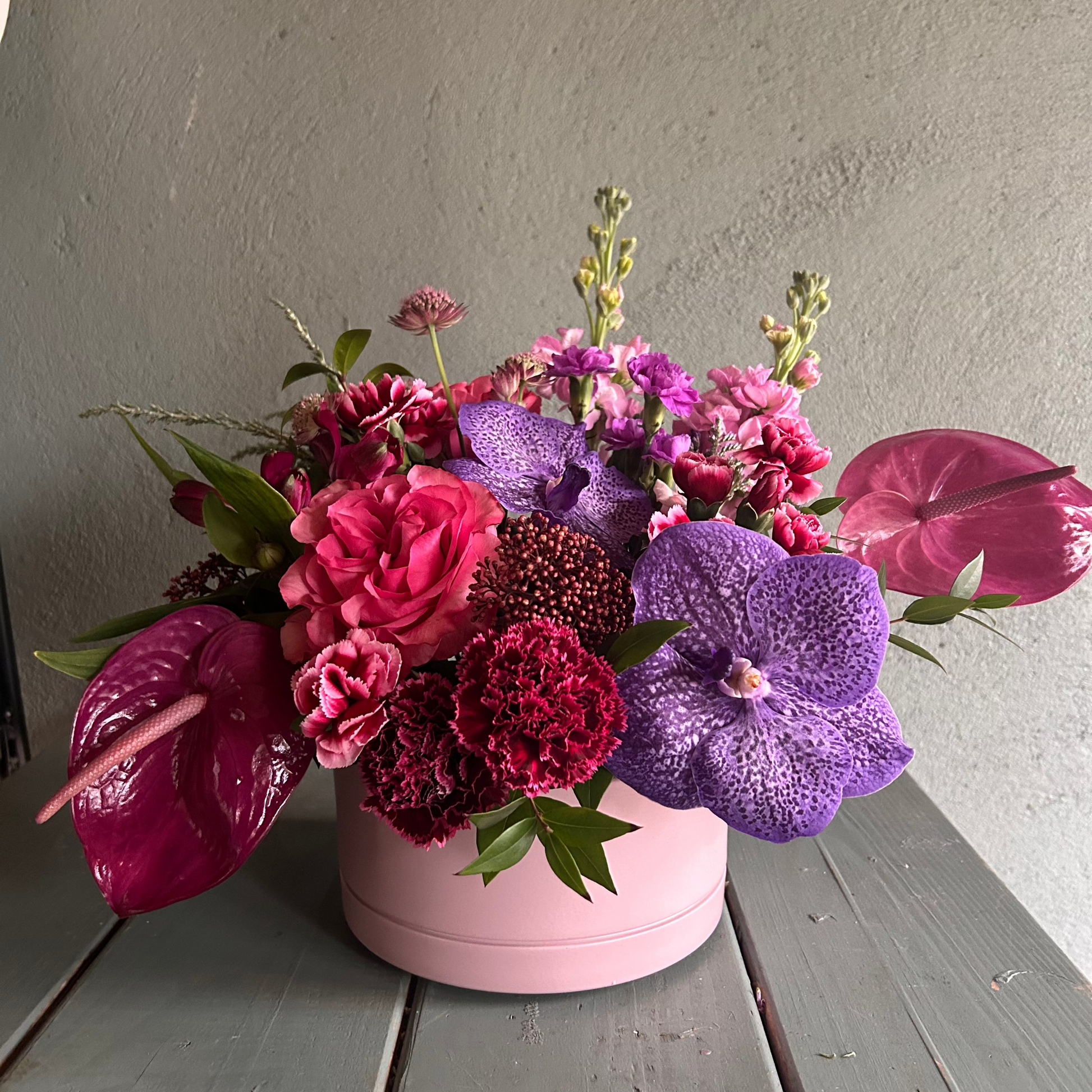 Colorful flower arrangement in a pink pot on a wooden surface with a gray background