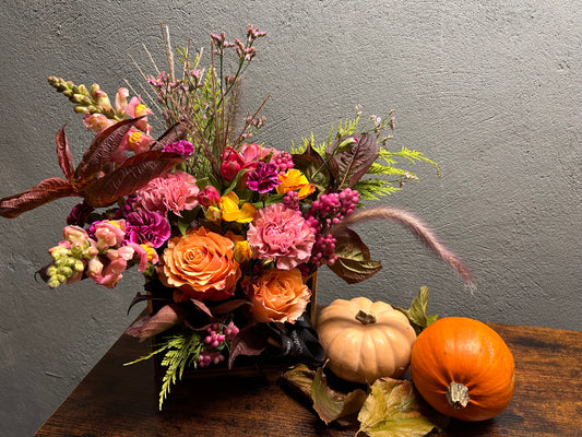 Send a Hug - Autumn Edition arrangement with vibrant flowers and pumpkins on a wooden table.